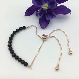 May include: A black bead bracelet with a rose gold adjustable slider clasp. The bracelet is made of black onyx beads and has a rose gold chain.