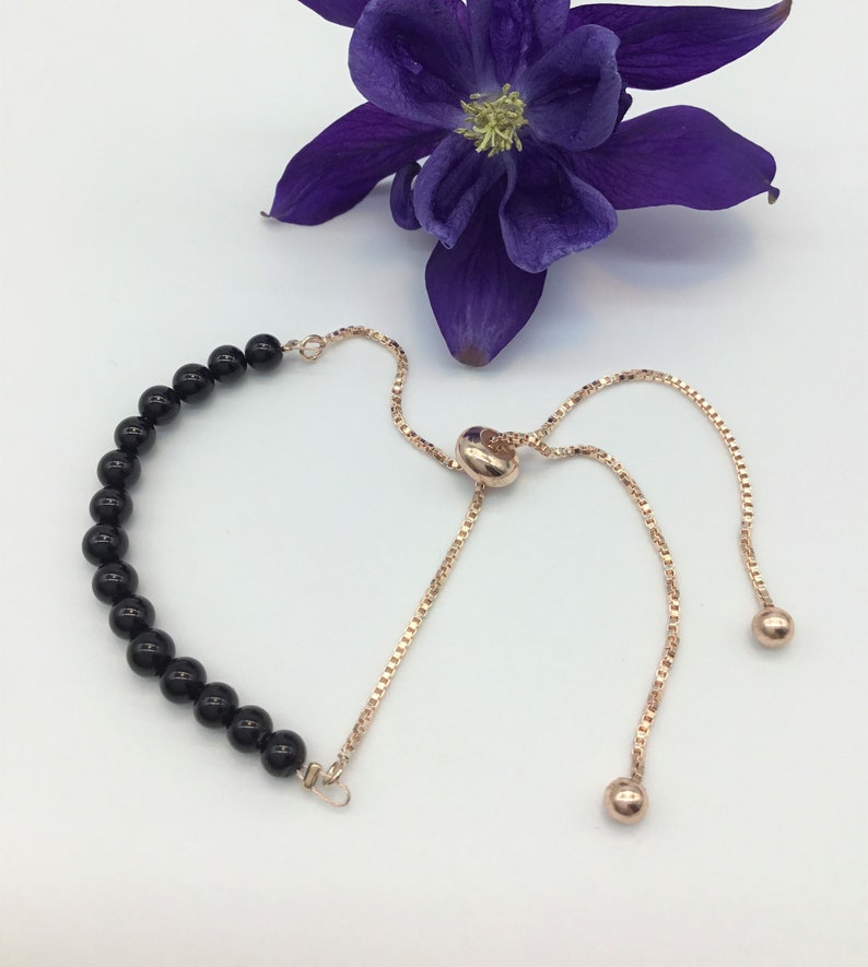 May include: A black bead bracelet with a rose gold adjustable slider clasp. The bracelet is made of black onyx beads and has a rose gold chain.