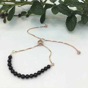 May include: A black onyx beaded bracelet with a rose gold adjustable slider clasp. The bracelet is made with round black onyx beads and a rose gold chain.