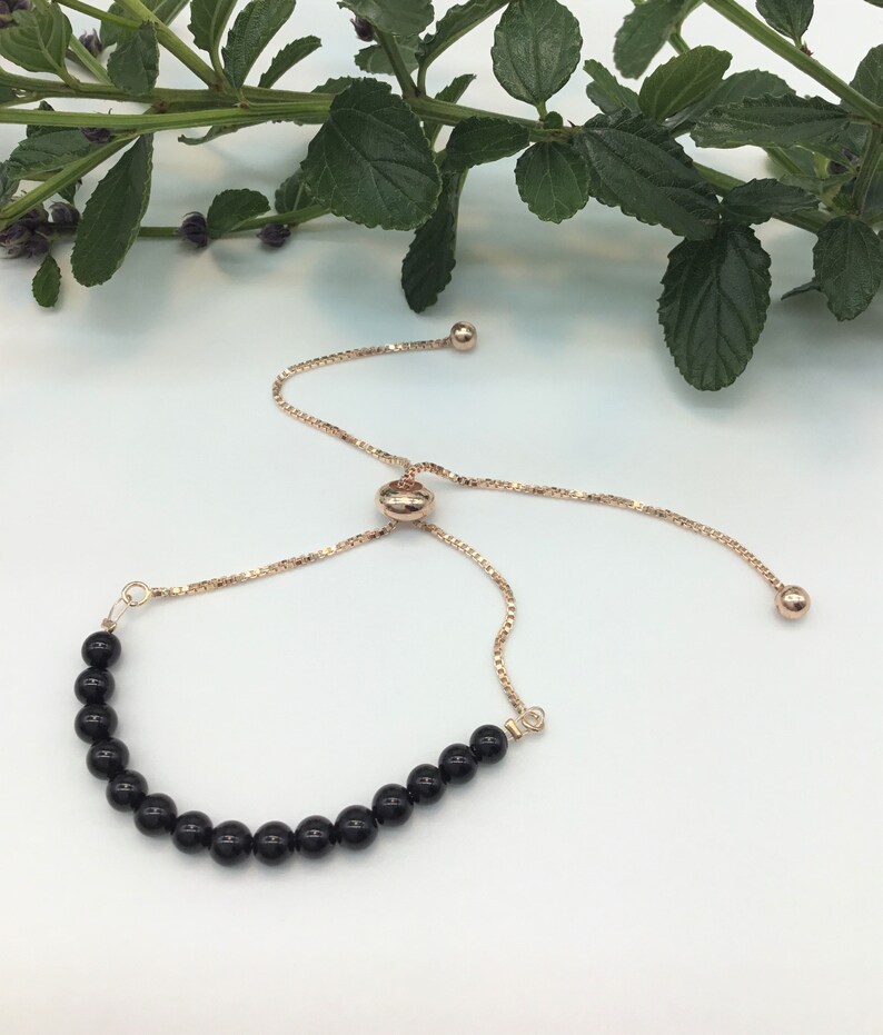 May include: A black onyx beaded bracelet with a rose gold adjustable slider clasp. The bracelet is made with round black onyx beads and a rose gold chain.