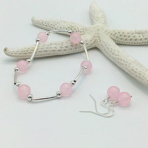 May include: A set of pink gemstone earrings and a bracelet. The earrings are silver with pink round beads. The bracelet is silver with pink round beads and a silver bar.