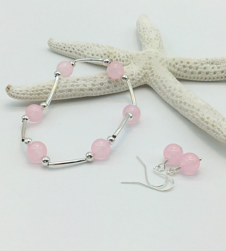 May include: A set of pink gemstone earrings and a bracelet. The earrings are silver with pink round beads. The bracelet is silver with pink round beads and a silver bar.