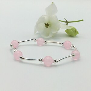 May include: A delicate bracelet with a silver chain and pink beads. The bracelet is on a white background with a white flower.
