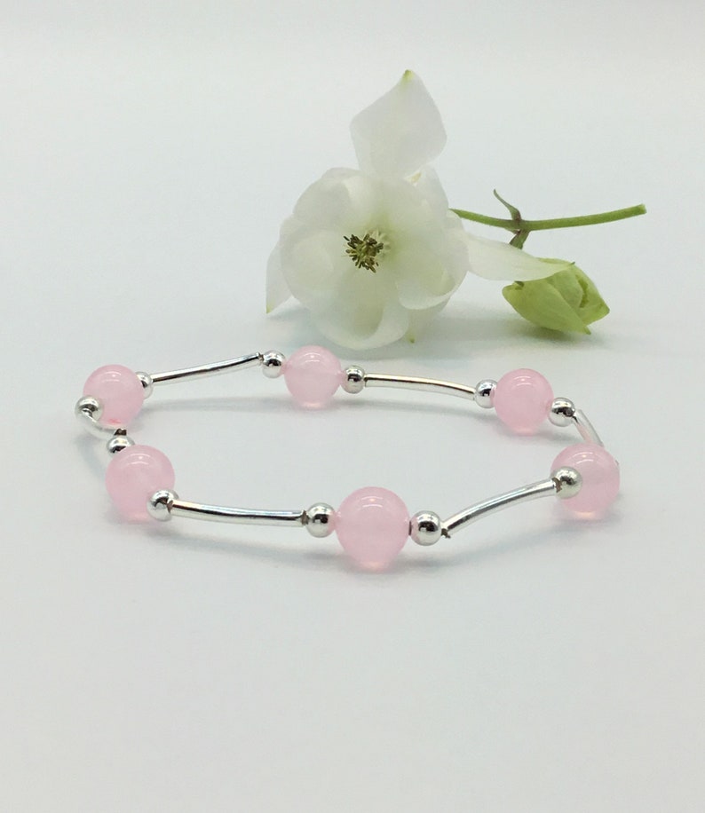 May include: A delicate bracelet with a silver chain and pink beads. The bracelet is on a white background with a white flower.