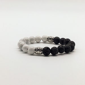 May include: A black and white beaded bracelet with silver accents. The bracelet is made with white howlite beads and black lava rock beads.