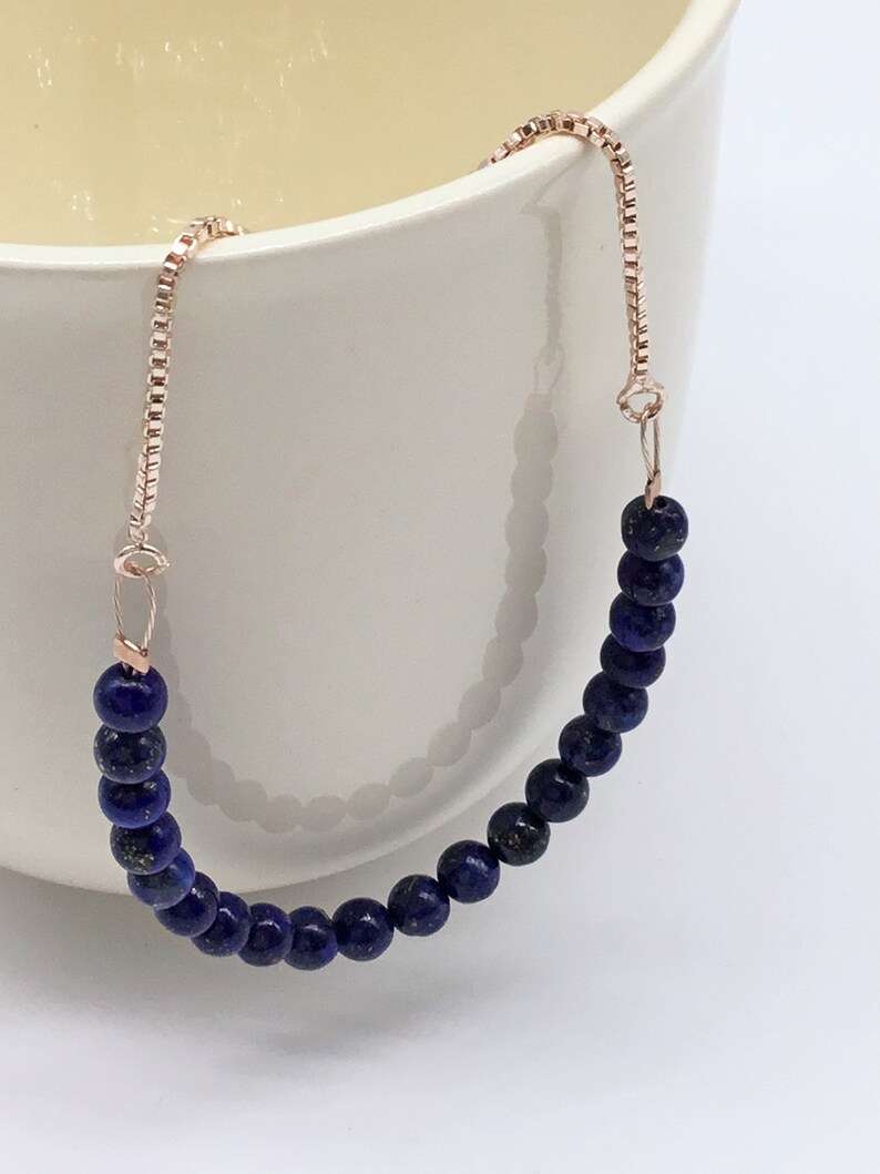 May include: A delicate bracelet made with dark blue lapis lazuli beads and a rose gold chain.