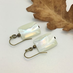 May include: A pair of iridescent white rectangular earrings with bronze hooks.
