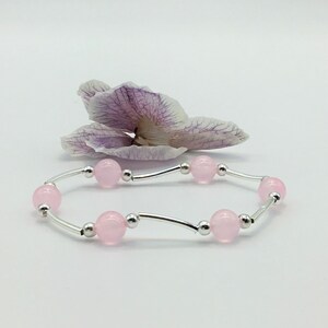 May include: A delicate bracelet with a silver chain and pink beads. The bracelet is displayed on a white background with a dried orchid flower.