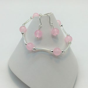 May include: A set of pink gemstone earrings and a bracelet. The earrings are silver with a pink gemstone dangle. The bracelet is silver with pink gemstones and a delicate chain.