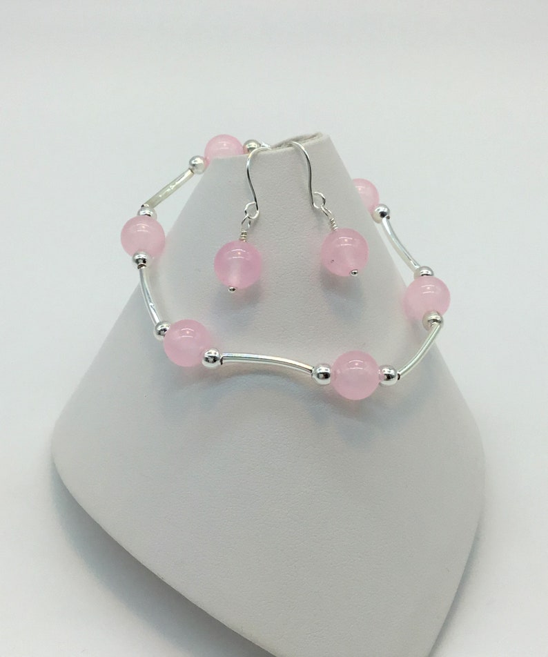 May include: A set of pink gemstone earrings and a bracelet. The earrings are silver with a pink gemstone dangle. The bracelet is silver with pink gemstones and a delicate chain.