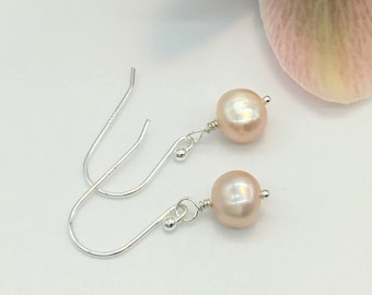 May include: A pair of silver dangle earrings with a single blush pink pearl on each earring.