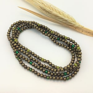 May include: A multi-strand necklace made of small, round, metallic beads in a bronze color. The necklace is accented with small, green and light green beads.