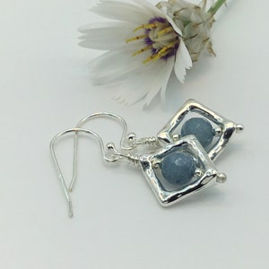 Op de afbeelding: Zilveren oorbellen met een blauwe edelsteen in een vierkant frame. De oorbellen hebben een eenvoudige haaksluiting.