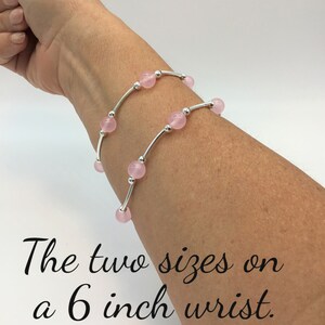 May include: Two silver bracelets with pink beads on a 6 inch wrist. The bracelets are layered on top of each other.