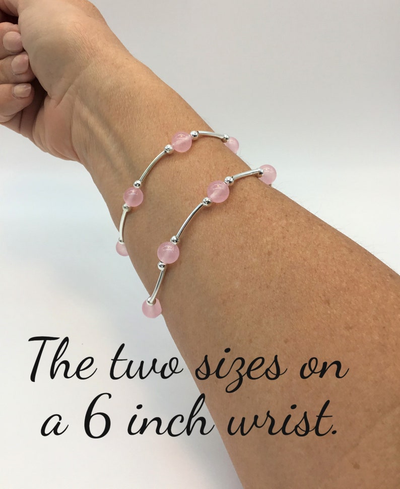 May include: Two silver bracelets with pink beads on a 6 inch wrist. The bracelets are layered on top of each other.
