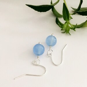 May include: A pair of silver earrings with light blue round beads.