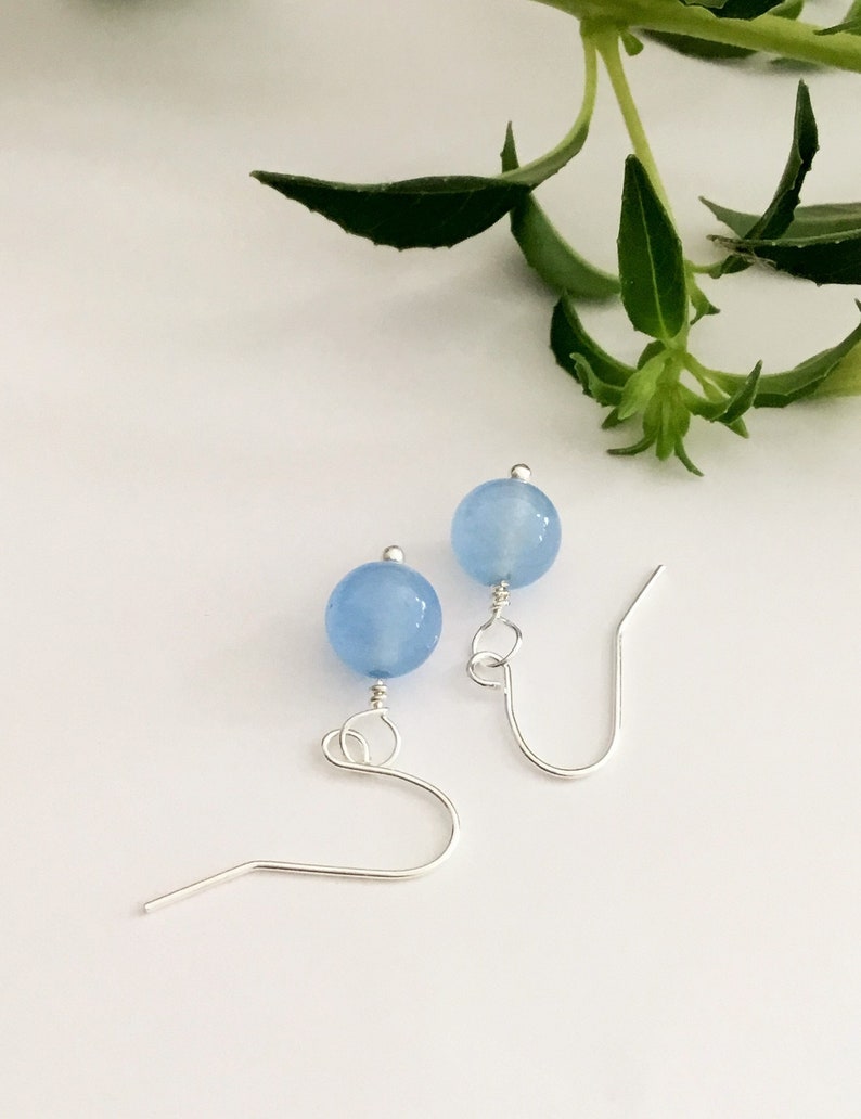 May include: A pair of silver earrings with light blue round beads.