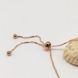 May include: A rose gold adjustable bracelet with a delicate chain and a small round bead at each end.
