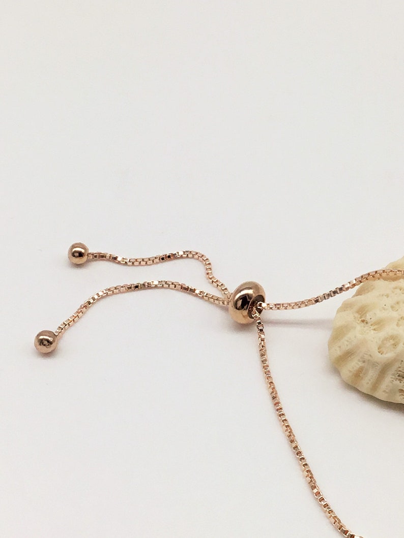 May include: A rose gold adjustable bracelet with a delicate chain and a small round bead at each end.