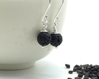 May include: A pair of silver earrings with black lava rock beads. The earrings are hanging from a white bowl.