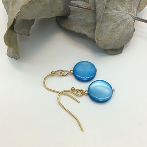 May include: A pair of gold earrings with blue round gemstone accents. The earrings have a simple design and are perfect for everyday wear.