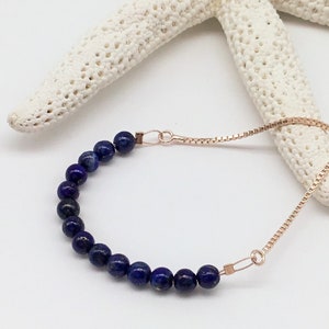 May include: A delicate bracelet with a chain made of rose gold and a row of dark blue lapis lazuli beads.