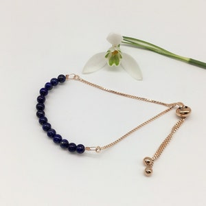 May include: A delicate adjustable bracelet with a row of dark blue lapis lazuli beads and a rose gold chain.