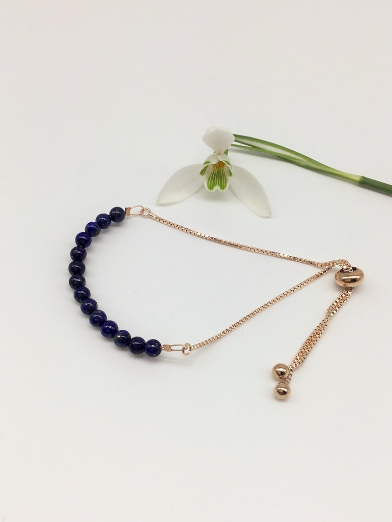 May include: A delicate adjustable bracelet with a row of dark blue lapis lazuli beads and a rose gold chain.