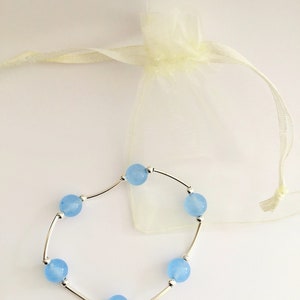 May include: A delicate bracelet with light blue beads and silver connectors. The bracelet is displayed on a white background with a white organza bag.