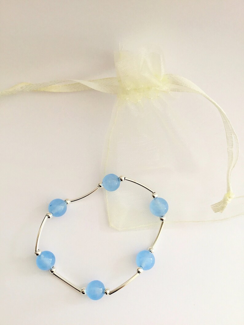 May include: A delicate bracelet with light blue beads and silver connectors. The bracelet is displayed on a white background with a white organza bag.