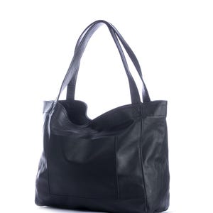 May include: A black leather tote bag with two long handles and a large front pocket. The bag has a simple, classic design and is made of a soft, textured leather. The bag is empty and stands upright against a white background.