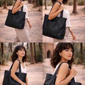 May include: A black leather tote bag with a front pocket and shoulder straps. The bag is rectangular and appears to be empty. The bag is being carried by a person in a white top and tan pants.