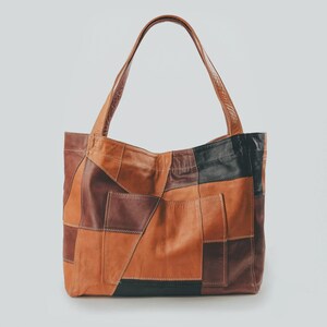 Peut inclure: Un sac fourre-tout en cuir patchwork dans les tons marron, beige et noir. Le sac a une forme rectangulaire avec deux anses et une poche sur le devant. Le sac est fait de différentes pièces de cuir cousues ensemble.
