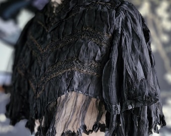 May include: A black sheer lace shawl with a ruffled trim and intricate embroidery. The shawl is draped over a dress form.