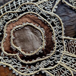 May include: Close-up of a brown leather surface with intricate white lace embroidery. The lace forms a circular pattern with a smaller circle in the center.