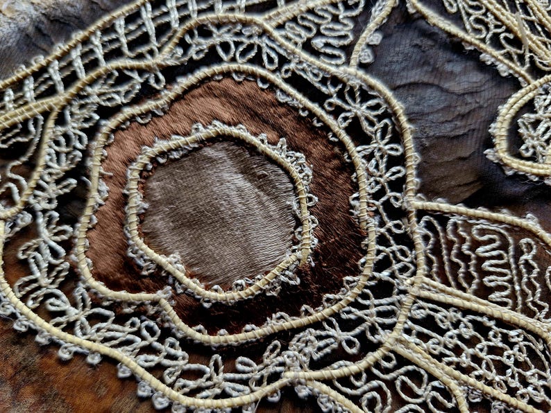 May include: Close-up of a brown leather surface with intricate white lace embroidery. The lace forms a circular pattern with a smaller circle in the center.