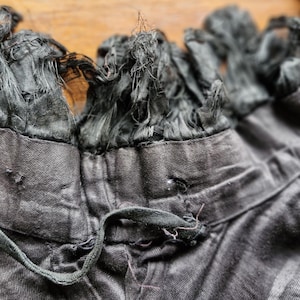 May include: A black garment with a frayed, black trim around the neckline. The garment has a drawstring at the neckline.