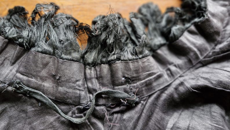 May include: A black garment with a frayed, black trim around the neckline. The garment has a drawstring at the neckline.