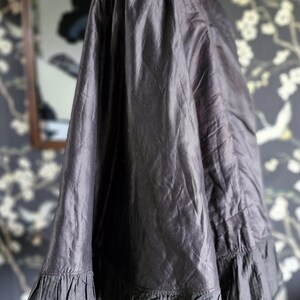 May include: A black silk cape with a ruffled trim. The cape is draped over a mannequin and has a high collar.