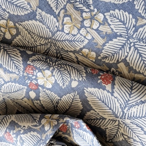 May include: A close-up of a blue and white fabric with a repeating pattern of leaves and berries. The fabric has a textured surface and a slightly faded look.