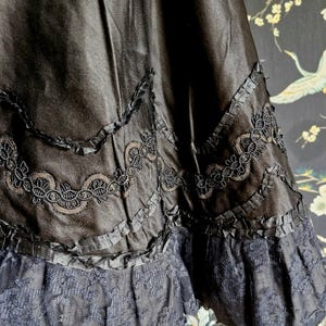 May include: Black satin skirt with a layered ruffle trim and black lace edging. The skirt has a scalloped design with a delicate black embroidery.
