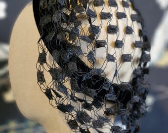 Può includere: Un cappello nero vintage con veletta, esposto su una testa di manichino. Il cappello presenta una fascia in velluto e una delicata rete tessuta che ricopre il viso. Il colore scuro e il design intricato suggeriscono uno stile formale o retrò.
