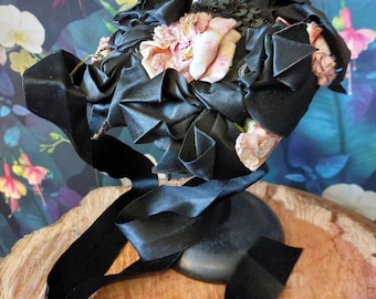May include: A black satin ribbon hat with pink fabric flowers and black sequins.