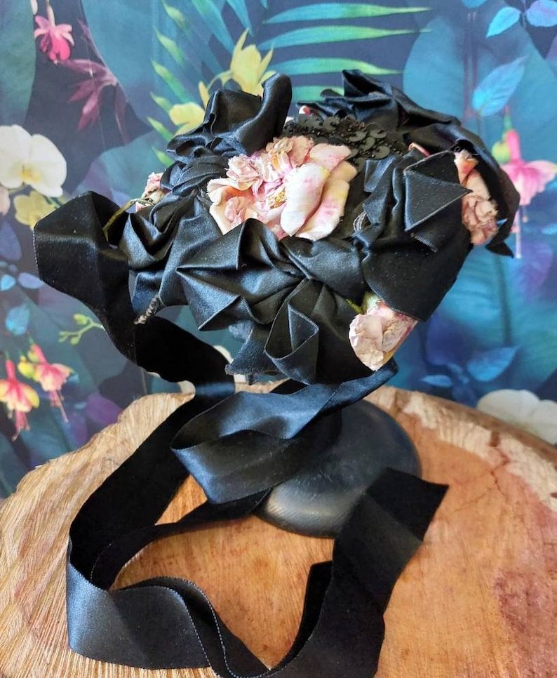 Pu&ograve; includere: Un cappello di nastro di raso nero con fiori di tessuto rosa e paillettes nere.
