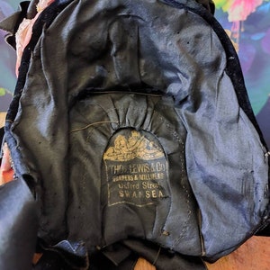Pu&ograve; includere: Un cappello di velluto nero con un'etichetta dorata che recita "THOS. LEWIS & CO. DRAPERS & MILLINERS Oxford Street SWANSEA."