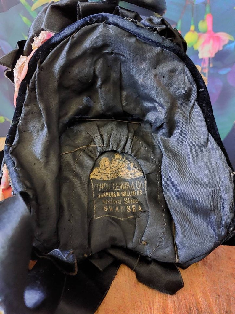 Pu&ograve; includere: Un cappello di velluto nero con un'etichetta dorata che recita "THOS. LEWIS & CO. DRAPERS & MILLINERS Oxford Street SWANSEA."
