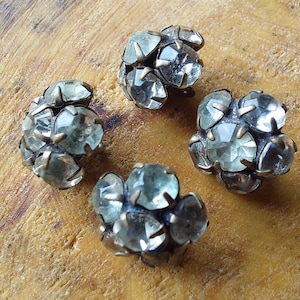 May include: Four silver-toned metal buttons with clear faceted glass stones. Each button has six stones arranged in a flower shape.