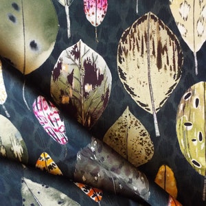 May include: A dark blue fabric with a repeating pattern of colourful leaves. The leaves are in shades of green, brown, yellow, and pink. The fabric has a subtle texture.