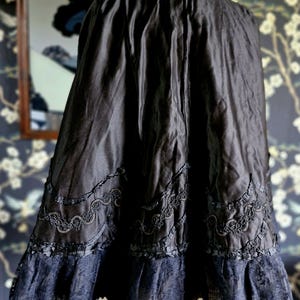 May include: A black satin cape with a high ruffled collar and lace trim. The cape is lined with black fabric and has a scalloped hem.