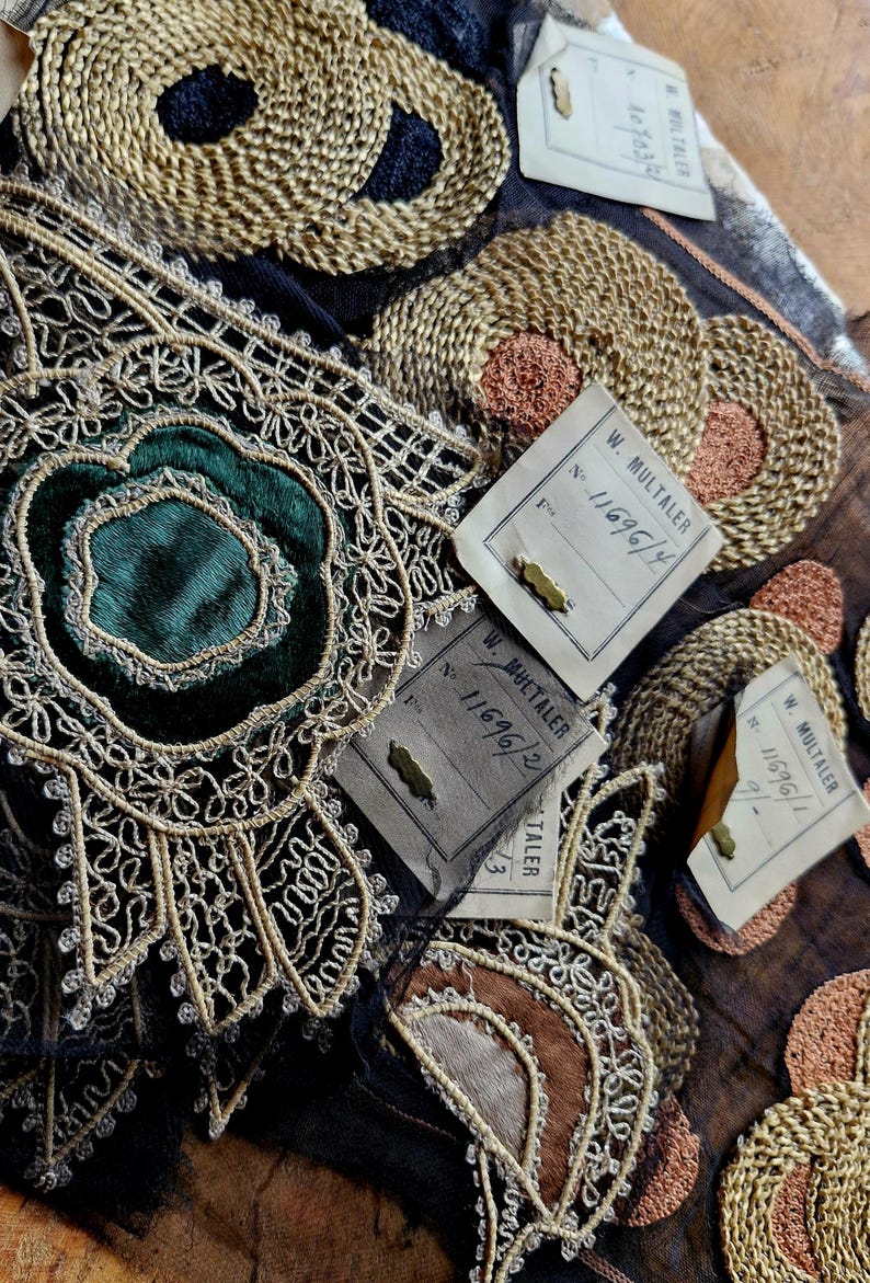 May include: Close-up of several antique fabric trims with gold and silver embroidery. The trims are on a black fabric background. There are three paper tags with the text "W. MULTALER" and numbers.